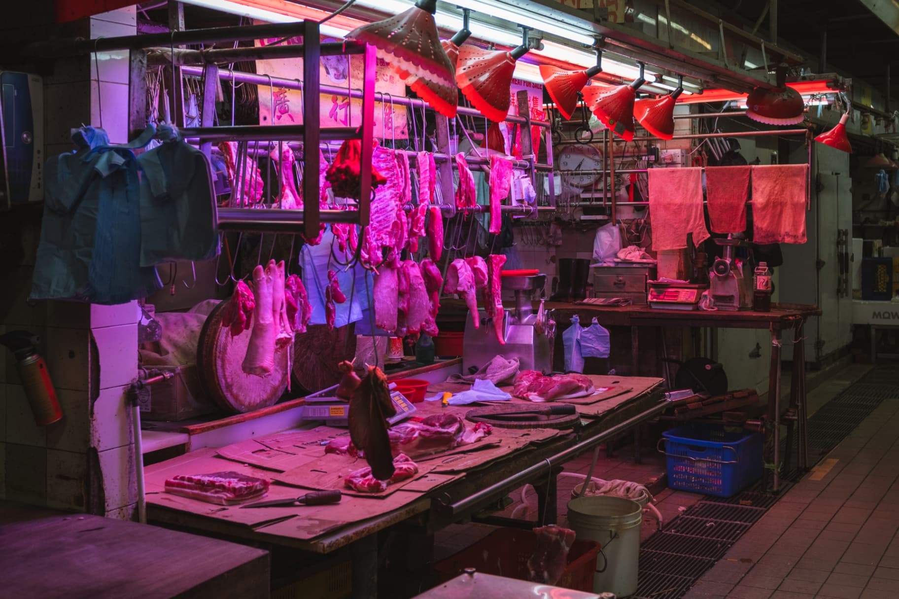 A traditional Hong Kong meat stall illuminated by vibrant red lamps with cuts of pork hanging from metal hooks.