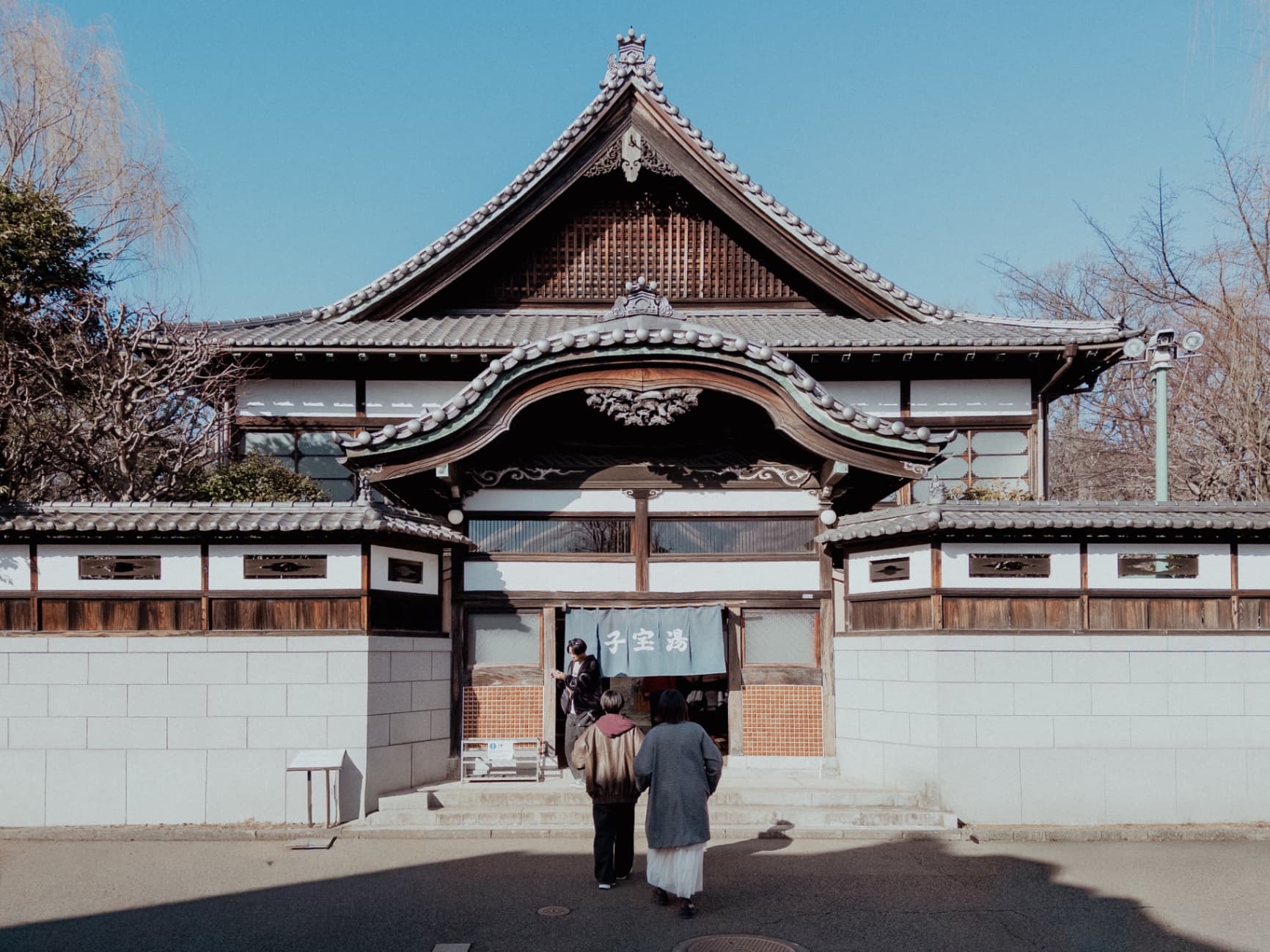 Front view of a traditional Japanese sento bathhouse with a curved tiled roof and a blue noren curtain.