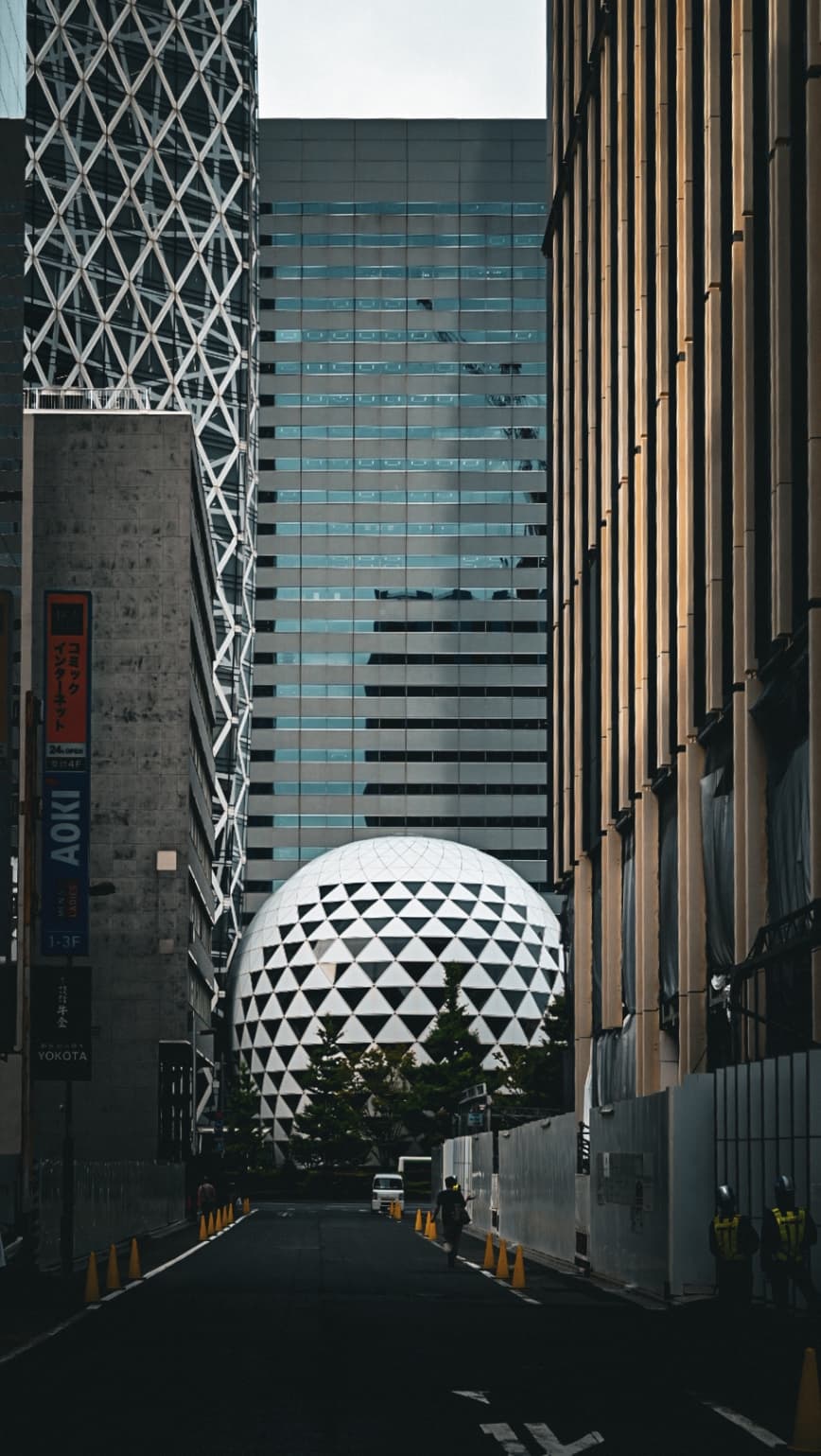 A large white dome with a black triangular pattern sits between two tall skyscrapers in Shinjuku, Tokyo.